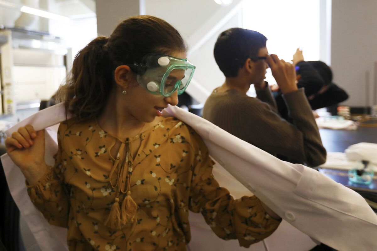 Mia Turel, 13, puts on her lab coat at the start of her chemistry lab. (Francine Orr / Los Angeles Times)