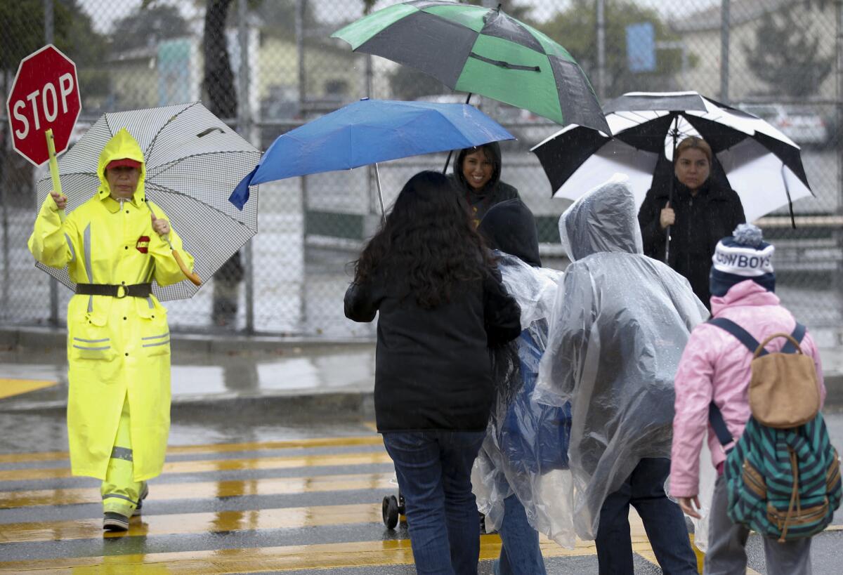 Crossing guard Maria Brito, left, escorts her pedestrians at Ford Boulevard and Verona Street in East Los Angeles during a morning rainstorm.