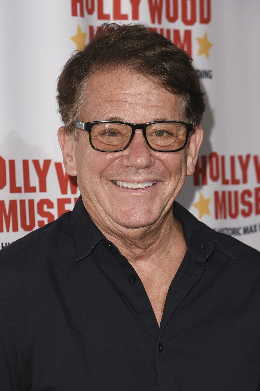 A smiling man in rectangular eyeglasses and black dress shirt