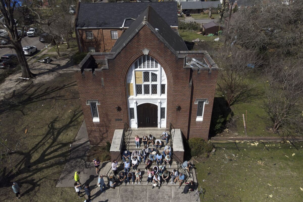 People worship on the steps of the Rolling Fork United Methodist Church, right, as damage is visible to surrounding properties, Sunday, March 26, 2023, in Rolling Fork, Miss. Emergency officials in Mississippi say several people have been killed by tornadoes that tore through the state on Friday night, destroying buildings and knocking out power as severe weather produced hail the size of golf balls moved through several southern states. (AP Photo/Julio Cortez)