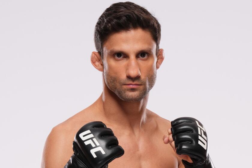 A shirtless fighter poses with his fists up, with the UFC logo on his gloves