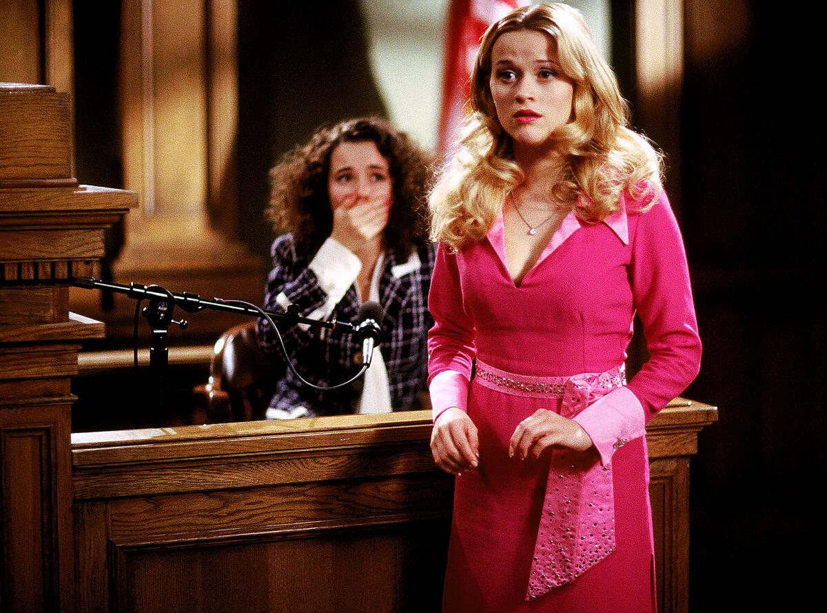 A woman in a pink dress speaks in a courtroom.