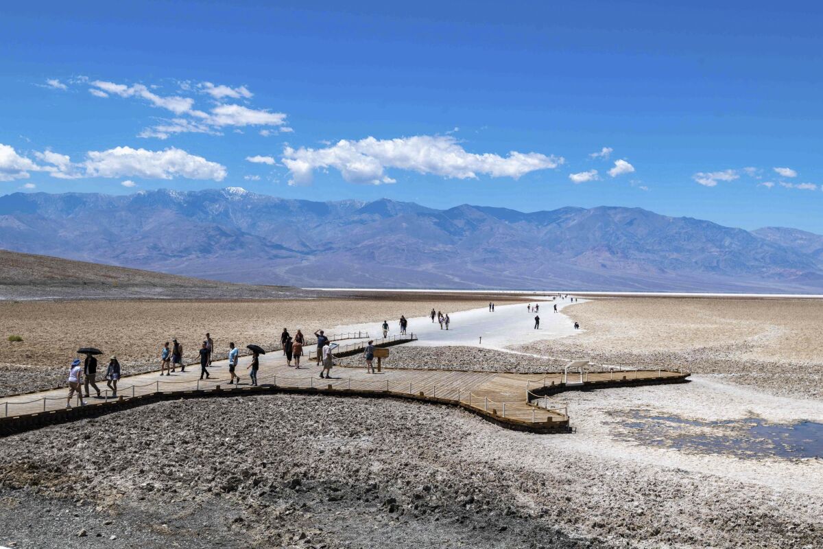 People walk through Badwater Basin, a dry lake bed, with mountains in the distance
