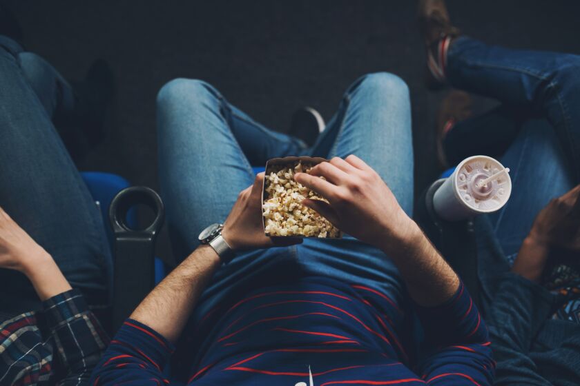 Unrecognizable young man watching the movie and eating popcorn in the cinema