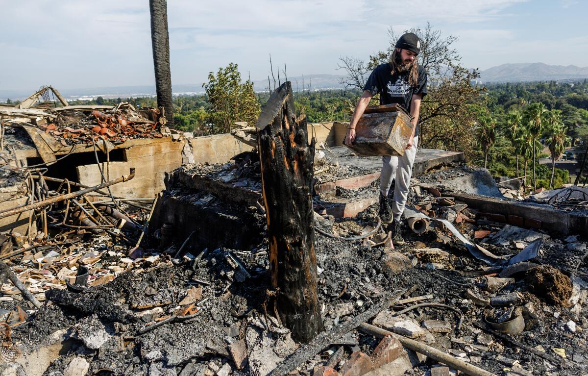 Aidan Milam removes a burned tool chest from the rubble of his destroyed home after the Edgehill fire burned his house.