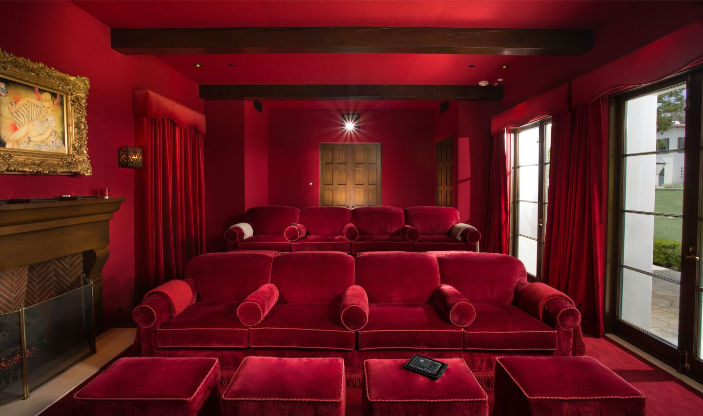 The movie theater with red walls and ceilings and chairs and tables, plus a fireplace.