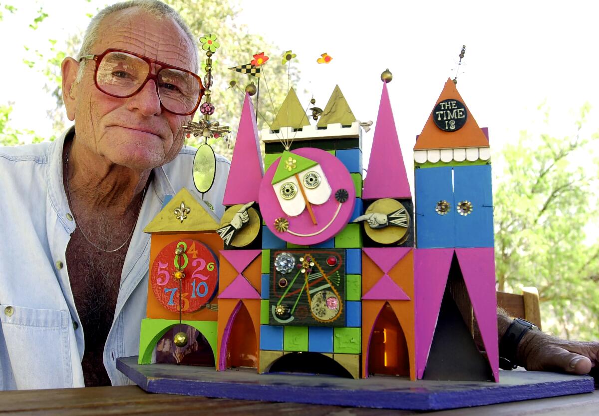 Rolly Crump beside a colorful mockup of the It's A Small World clock tower.