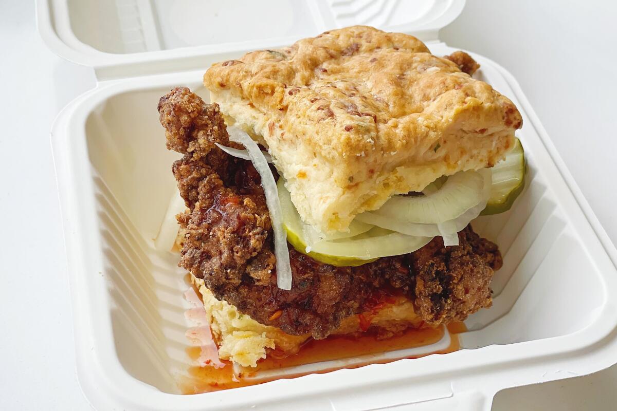 Fried chicken biscuit sandwich with hot honey, pickles and onions in a to-go container