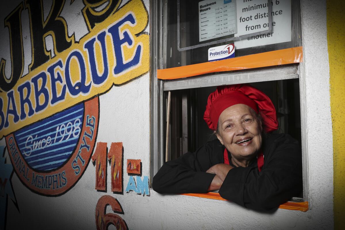  Jeanie Jackson, founder of JR's Barbecue, leans out of the take-out window in a red chef's hat. 
