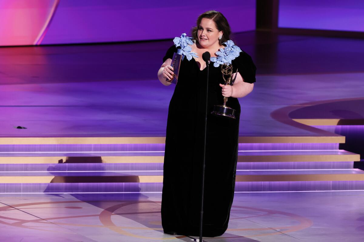 Woman in black dress with flowers holding an Emmy 