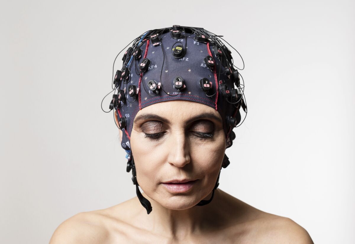 A woman is shown with a cap embedded with electrodes to measure brain activity.