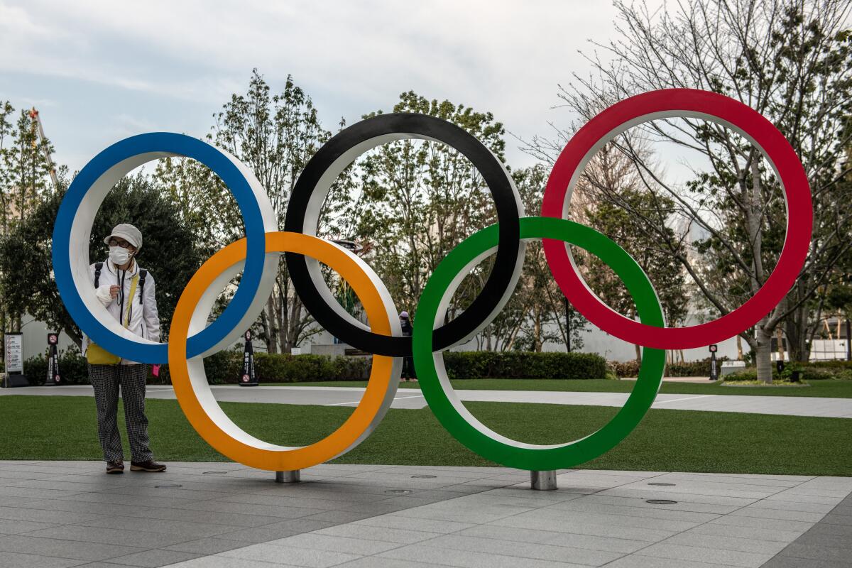 A woman wearing a face mask poses for a photograph next to a display of the Olympic rings in Tokyo on Friday.