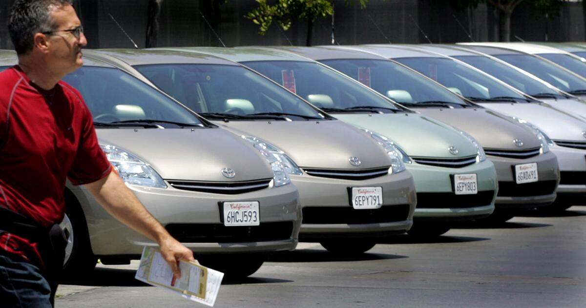A traveler walks by a line of Toyota cars parked at the Hertz's rental lot near Los Angeles International Airport. Rates for car rentals have dropped thanks to increased competition.