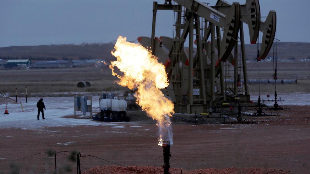 Workers tend to oil pump jacks behind a natural gas flare near Watford City, N.D., in October 2015.