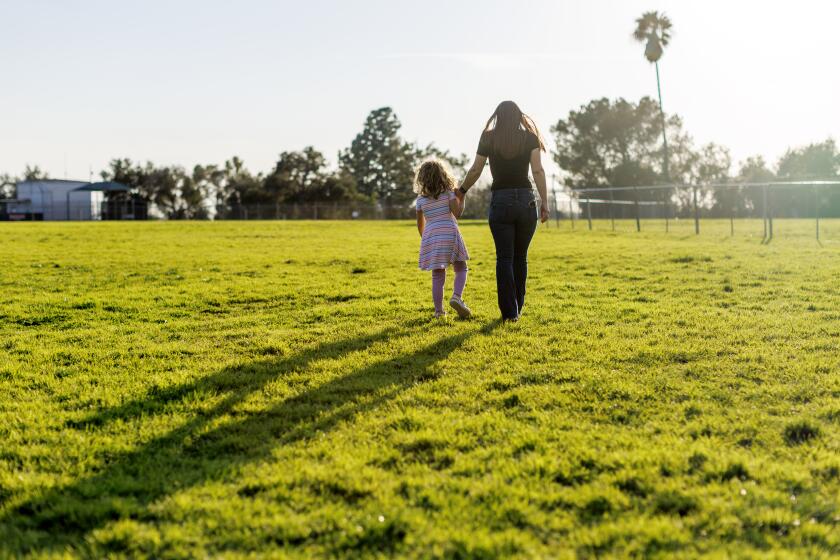 PASADENA, CA - FEBRUARY 14, 2024: Alexia Carbone walks hand-in-hand with her 5-year-old trans daughter "A." at a park near her home on February 14, 2024 in Pasadena, California. A's father Adam Vena his under a five-year restraining order as a result of a long custody and domestic violence case against him. He has alleged on social media that the order is a result of his not accepting A.'s transition, and rightwing activists have made him into a poster father for anti-trans causes. The case is much more complicated that that. ***WE CAN'T SHOW A's FACE, SO PLEASE DO NOT LIGHTEN PHOTO***(Gina Ferazzi / Los Angeles Times)