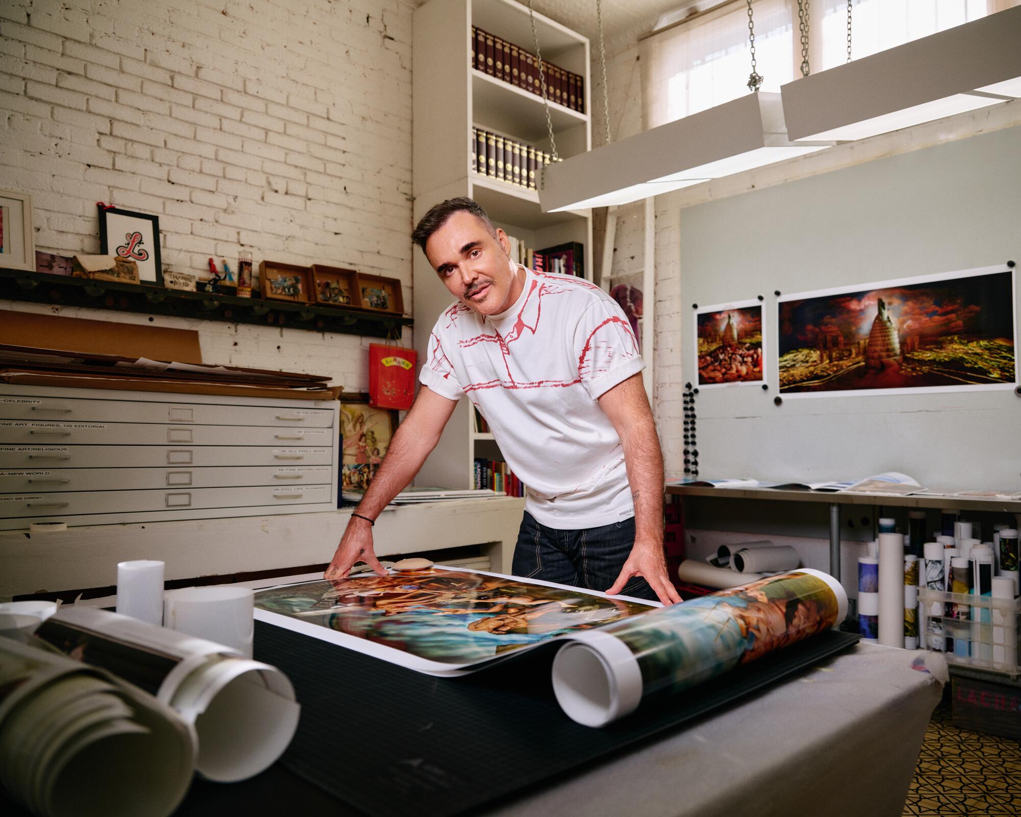 David LaChapelle stands behind a table with prints of his photographs.