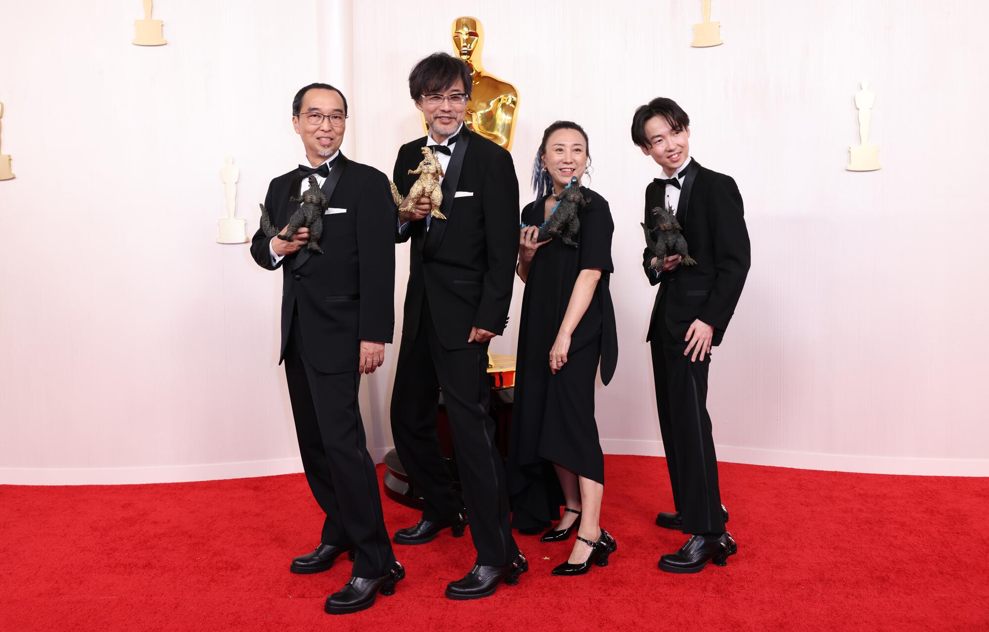 Three men and a woman pose with Godzilla toys.
