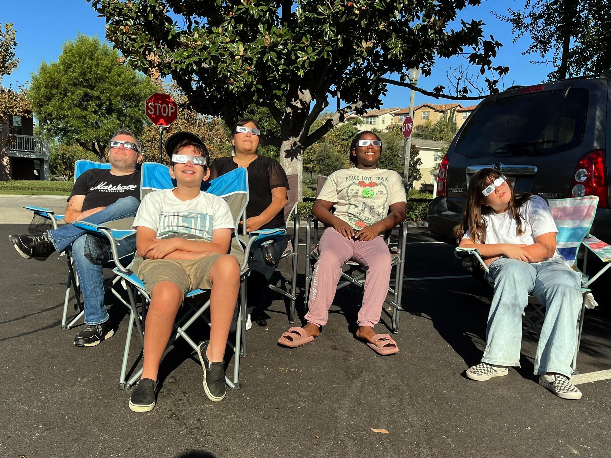 A family watches the eclipse from the parking lot in chairs.
