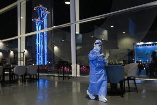 A workers wearing protective gear collects swab samples from tables and chairs for COVID testing at the main media center of the 2022 Winter Olympics, Thursday, Feb. 10, 2022, in Beijing. (AP Photo/Jae C. Hong)