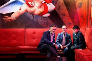 Three men sit on a red banquette with a mural of an airborne luchador over their shoulder. 
