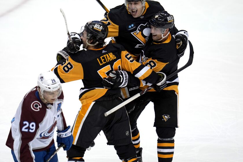 Pittsburgh Penguins' Kris Letang (58) celebrates his overtime goal with Evgeni Malkin (71) and Brian Dumoulin (8) as Colorado Avalanche's Nathan MacKinnon (29) skates off the ice, in an NHL hockey game in Pittsburgh, Tuesday, Feb. 7, 2023. (AP Photo/Gene J. Puskar)