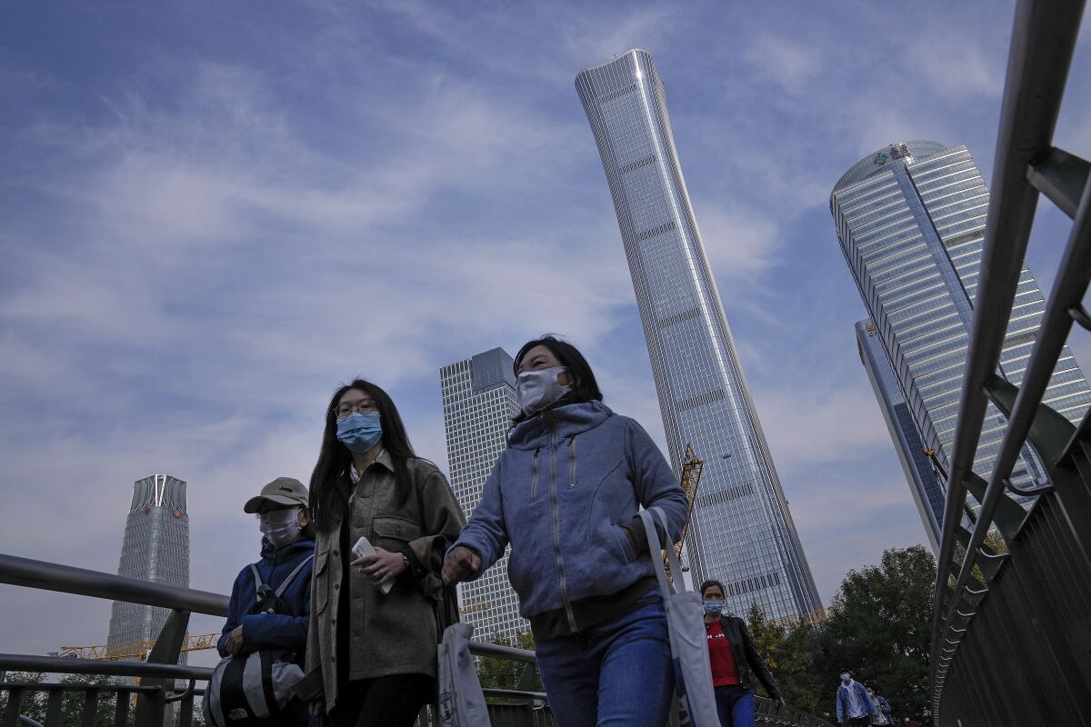 People wearing face masks to help protect from the coronavirus walk on a pedestrian overhead bridge past construction cranes at the Central Business District in Beijing, Monday, Oct. 18, 2021. China's economic growth sank in the latest quarter as a slowdown in construction and curbs on energy use weighed on its recovery from the coronavirus pandemic. (AP Photo/Andy Wong)