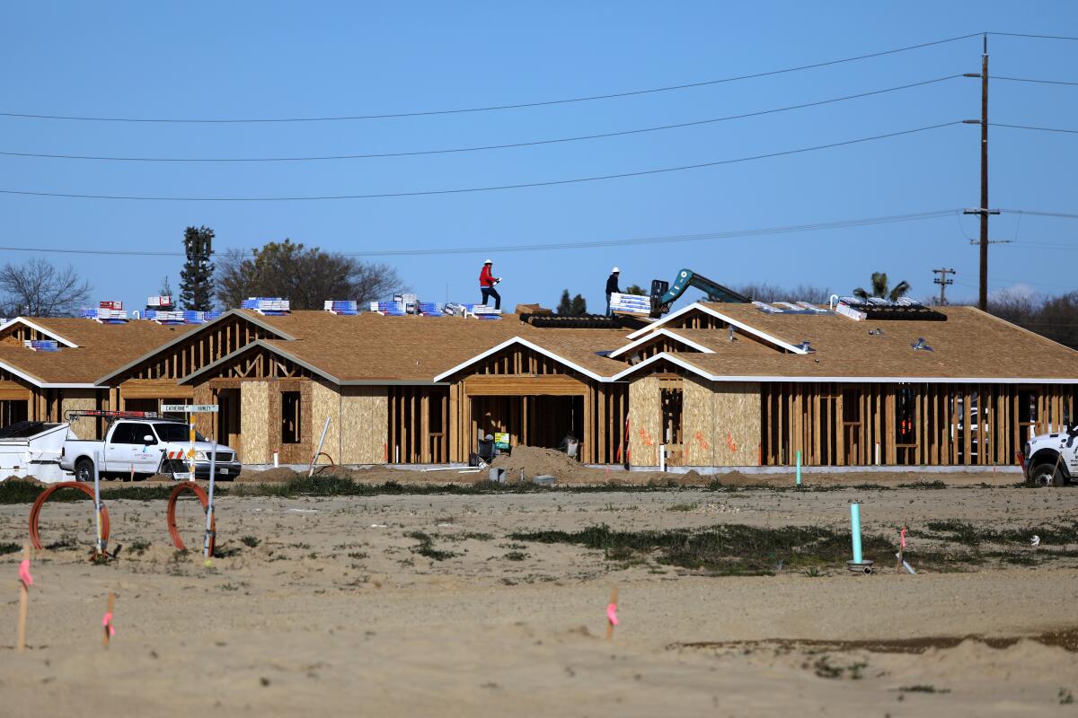 Homes are seen under construction with a dirt field in the foreground.
