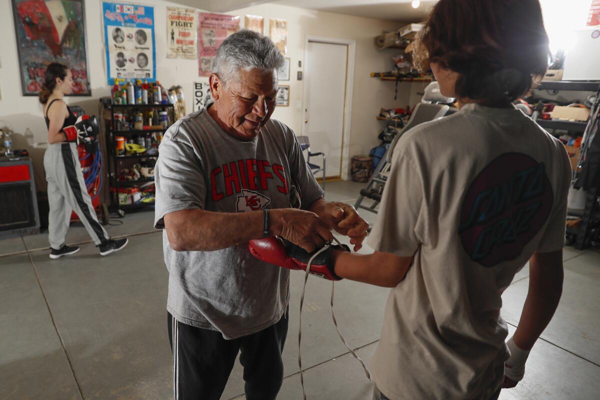 An older man helps a younger one lace up his boxing glove.