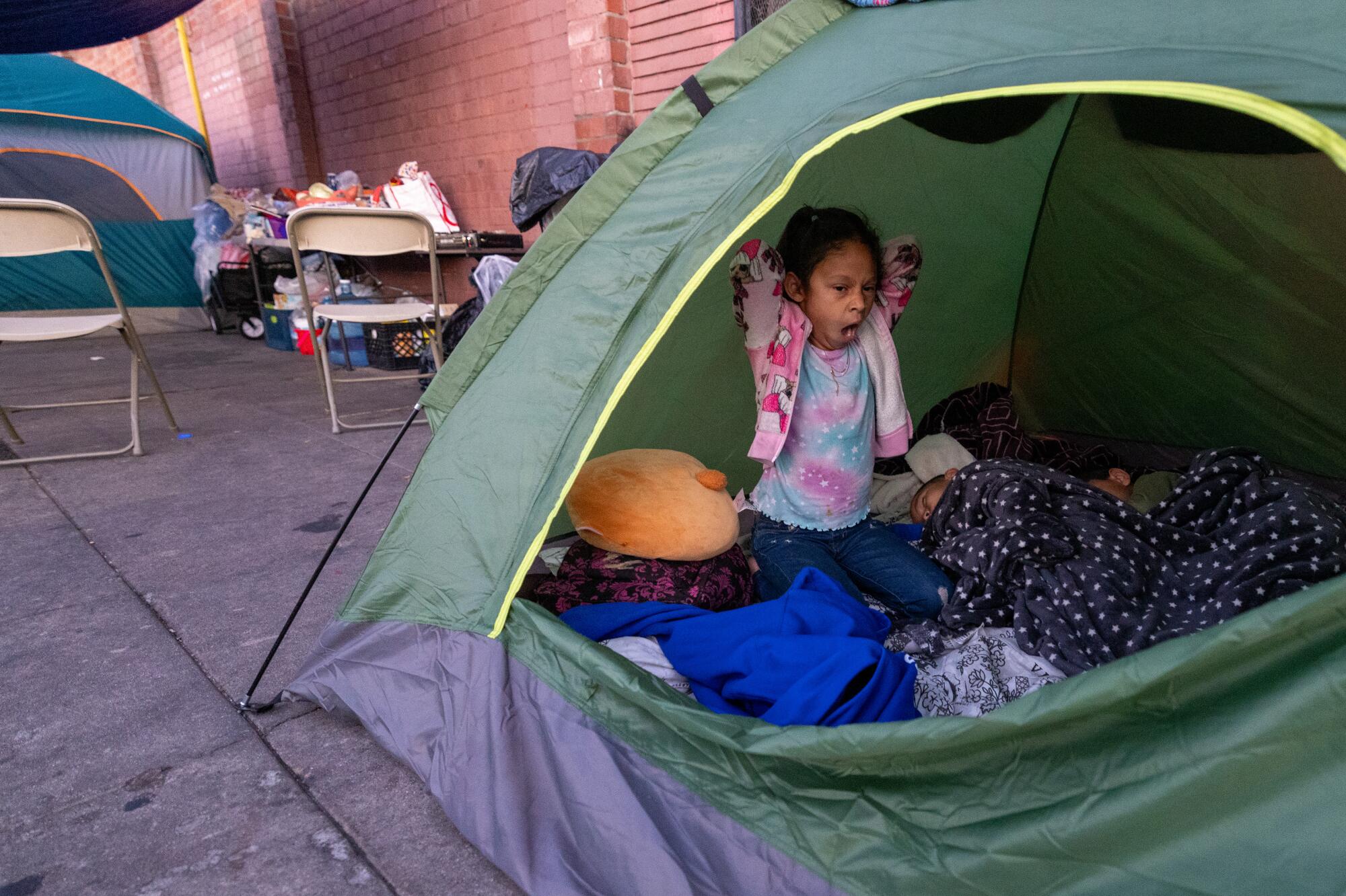A girl in a green tent on a sidewalk.