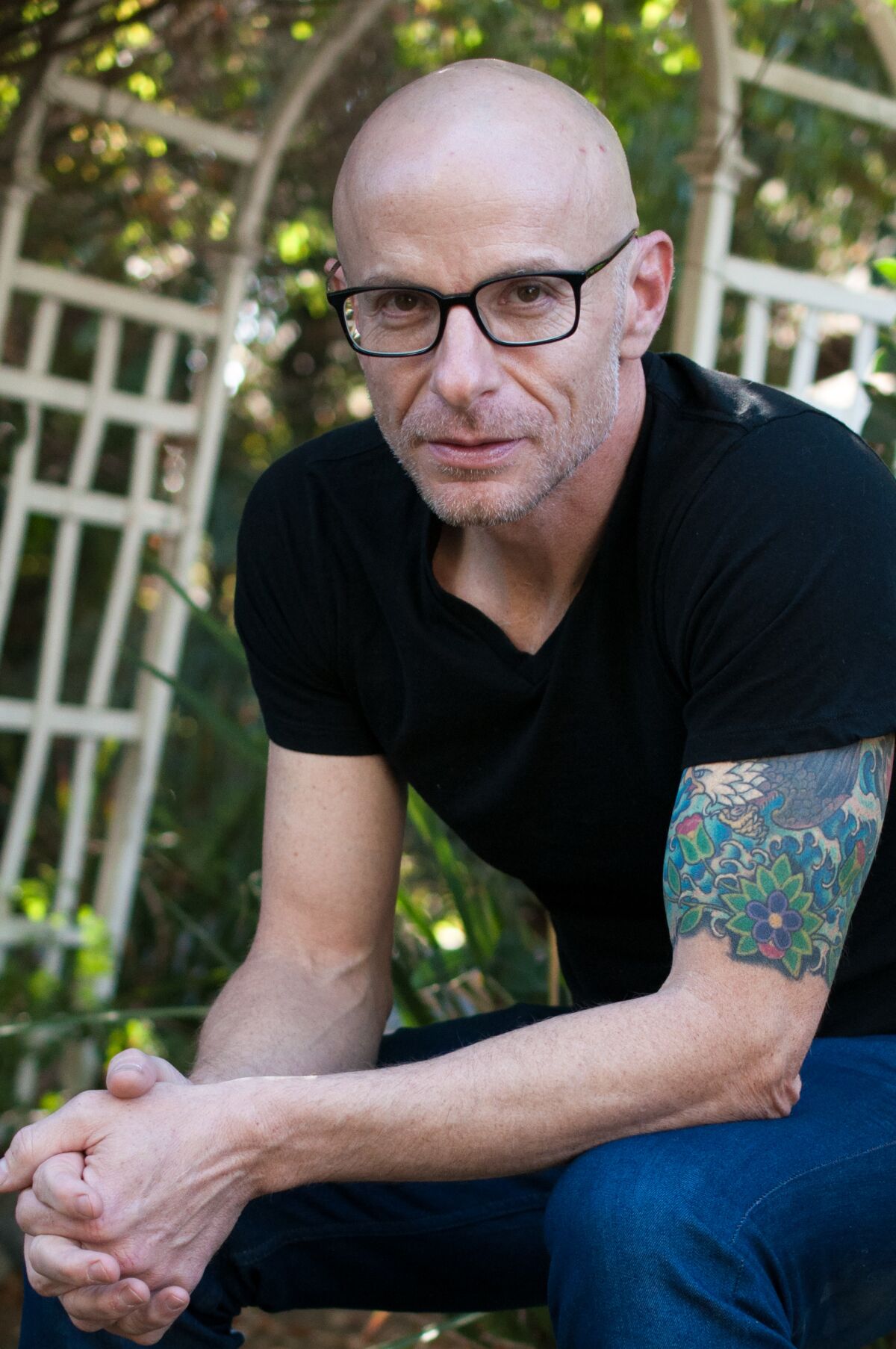 A photo portrait of a man with tattoos on his upper left arm and wearing a black T-shirt 