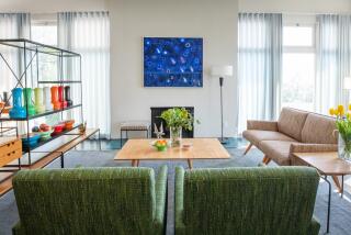 A view of a stylish living room with arm chairs with hairpin legs and a shelf room divider with colorful ceramics