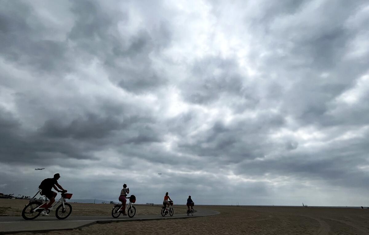 Bicyclists ride on a beach bike trail with dark clouds overhead