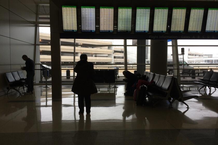 In a precursor of weekend delays, a traveler on Monday reads a flight tracking board showing numerous cancellations at Dallas-Fort Worth International Airport.