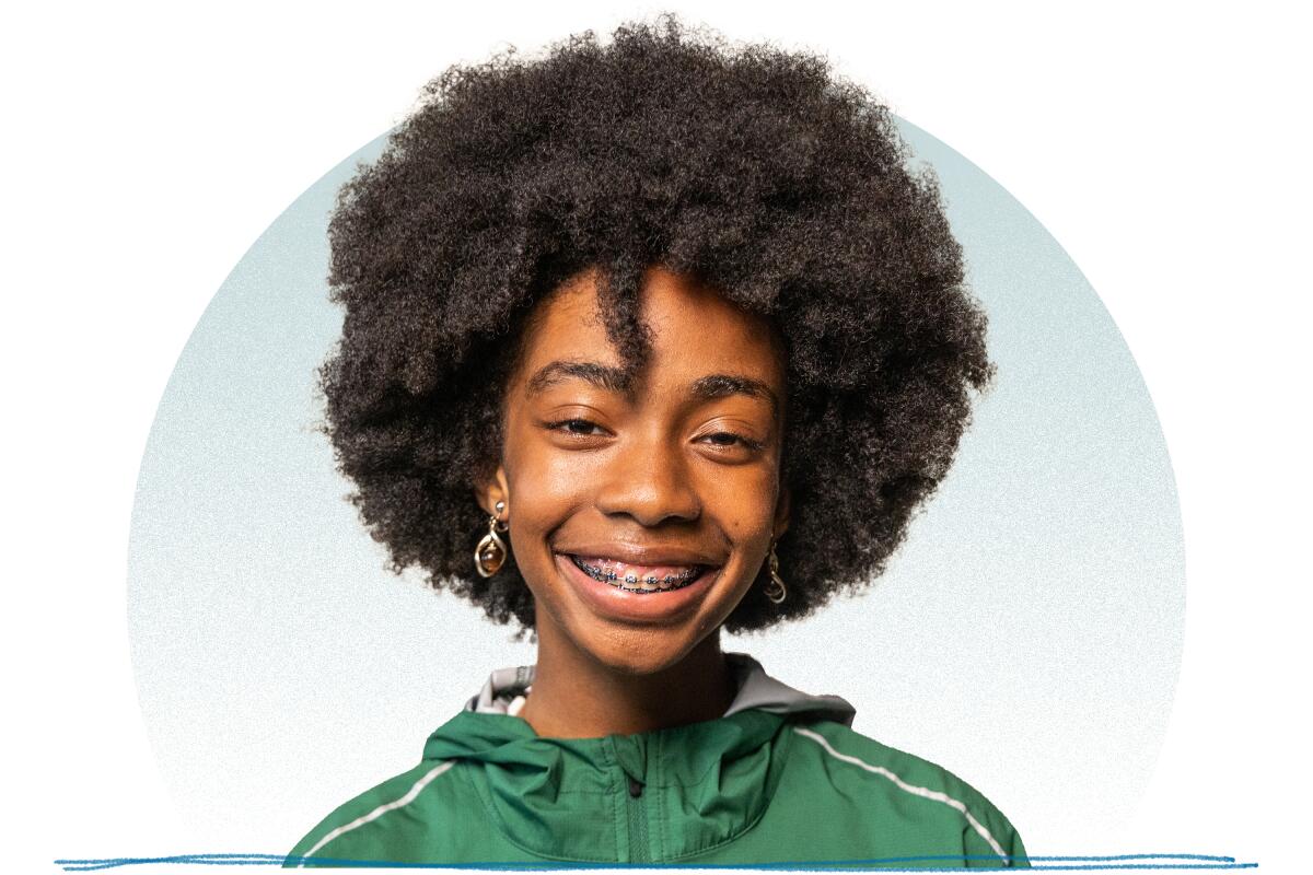 A young woman with a black afro, wearing a green jacket, with braces smiling for a portrait.
