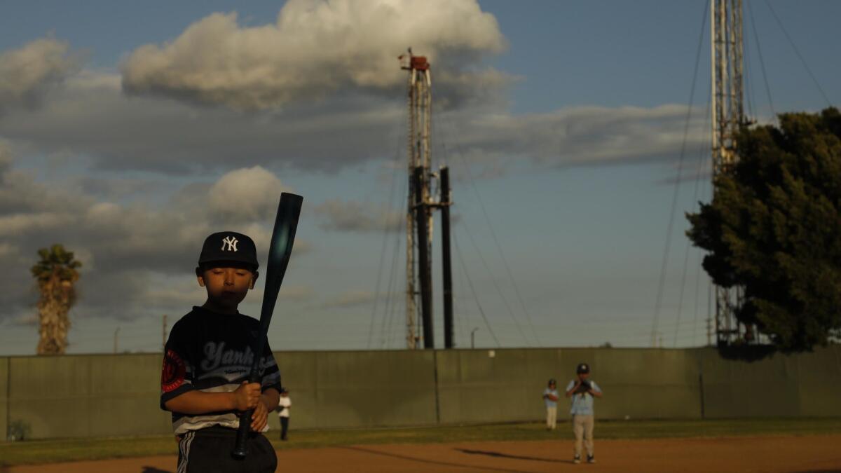 Benny Escobar, 7, stands at bat with two oil rigs towering in the background at John Mendez Baseball Park in Los Angeles' Wilmington neighborhood on April 16. Environmental groups are urging Gov. Gavin Newsom to ban fracking and to stop issuing new state permits for oil wells.