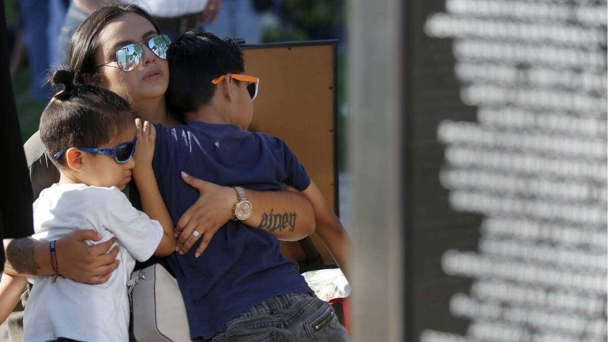 Tatiana Pineda, 27, of Irvine holds her children Mason Pineda, 4, left and Aiden Pineda, 6, as they sit next to a memorial in Northwood Community Park in Irvine. Her husband lost friends who served in Afghanistan. Their names are etched on the wall.