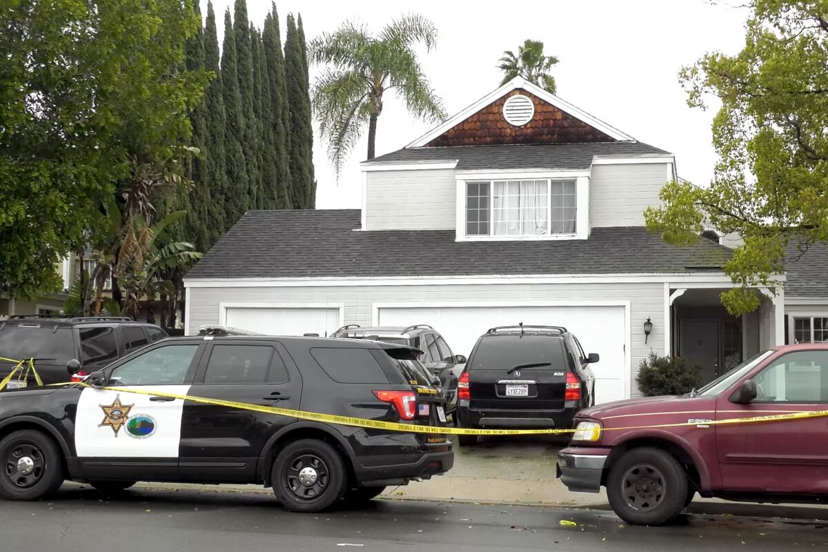 A two-story house with several cars, a police SUV and yellow crime-scene tape in front of it.