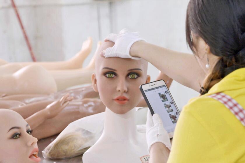 Factory worker inspecting the head of a sex doll during assembly.