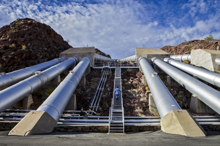 A man walks up stairs near giant pipes used for pumping water.