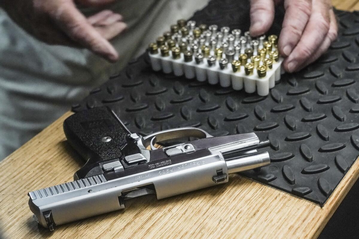 A pair of hands opens a box of ammunition on a counter next to a 9-millimeter semiautomatic handgun