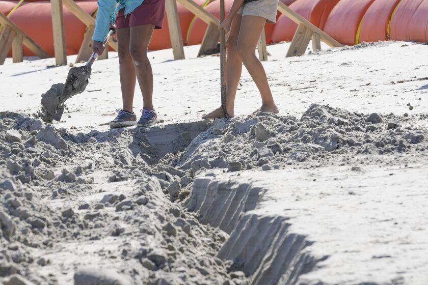 Las voluntarias Suzzanna Rogers, izquierda, y Olivia Storkamp, trabajan con arqueólogos para desenterrar una estructura expuesta de madera que se cree corresponde al naufragio de un barco de principios del siglo XIX en una playa, en Daytona Beach, Florida, el martes 6 de diciembre de 2022. (AP Foto/John Raoux)