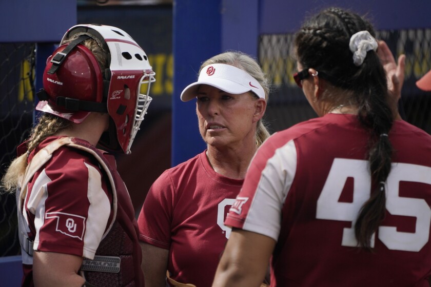 Oklahoma coach Patty Gasso, center, talks with catcher Lynnsie Elam, left and pitcher Giselle Juarez (45) during the team's NCAA Women's College World Series softball game against James Madison, Monday, June 7, 2021, in Oklahoma City. Gasso has been one of the most outspoken coaches regarding differences in scheduling and the quality of the facilities between the Women's College World Series and the men's baseball College World Series. (AP Photo/Sue Ogrocki)