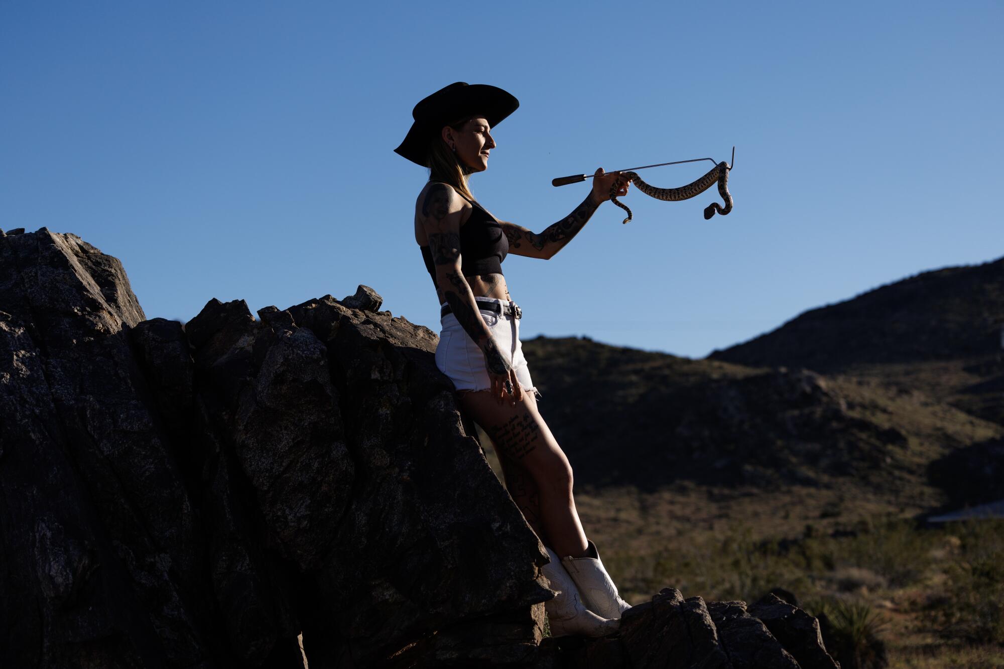Rattlesnake wrangler Danielle Wall, in a cowboy hat, holds a Southwestern speckled rattlesnake