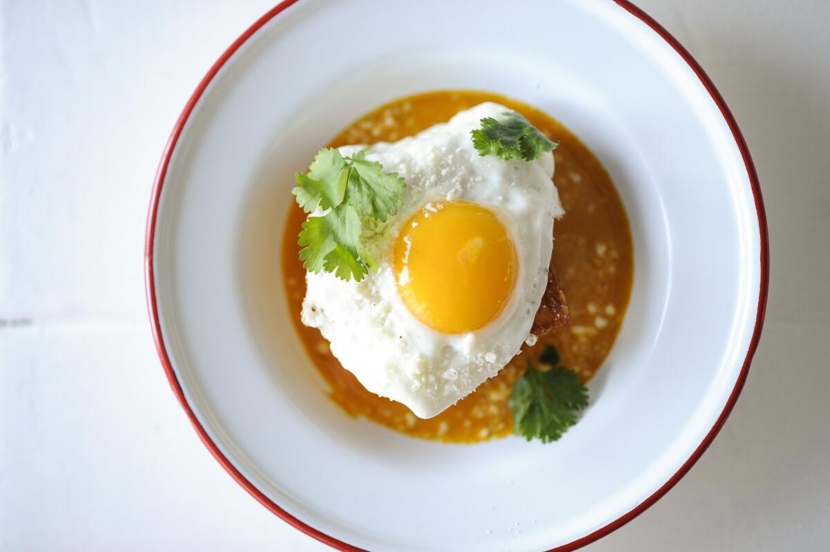 Crispy hash brown chilaquiles with sunny side up egg, cotija, and salsa macho is served at Trois Familia.