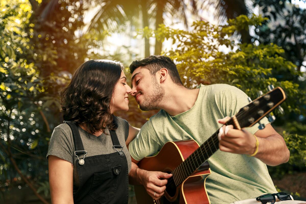  A couple is about to kiss as the man plays acoustic guitar for the woman.