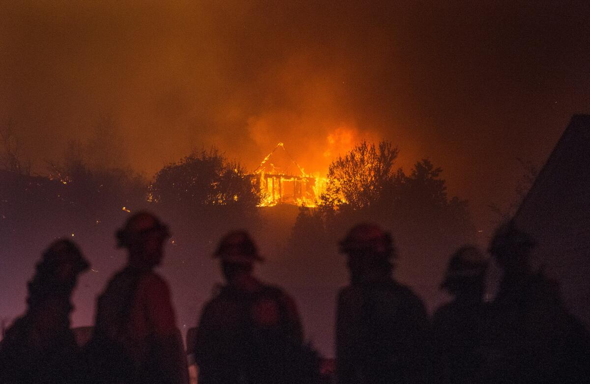 Forest Service fire fighters from Leavenworth watch as a house burns in northern Wenatchee, Wash., on June 28, 2015. A wildfire fueled by high temperatures and strong winds roared into a central Washington neighborhood, destroying properties and forcing residents of several hundred homes to flee, authorities said Monday.