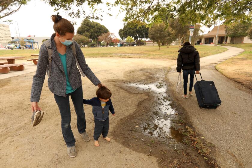 WESTCHESTER, CA - MAY 12, 2021 - - Stephanie Popescu and her son Dacian, 2 1/2 years old, head to the playground for a playdate with other children as a homeless woman walks by with her belongings in Westchester Park on May 13, 2021. Popescu, with Grass Roots Neighbors, bring food and supplies to homeless in the park twice a week. Grass Roots Neighbors is a volunteer community organization who meet the immediate needs of neighbors experiencing food and housing insecurity. Many homeless take residence in Westchester Park, one of several places recommended by Los Angeles City Councilman Mike Bonin as a safe camping/parking site for the homeless. Popecsu supports Bonin's plan. (Genaro Molina / Los Angeles Times)