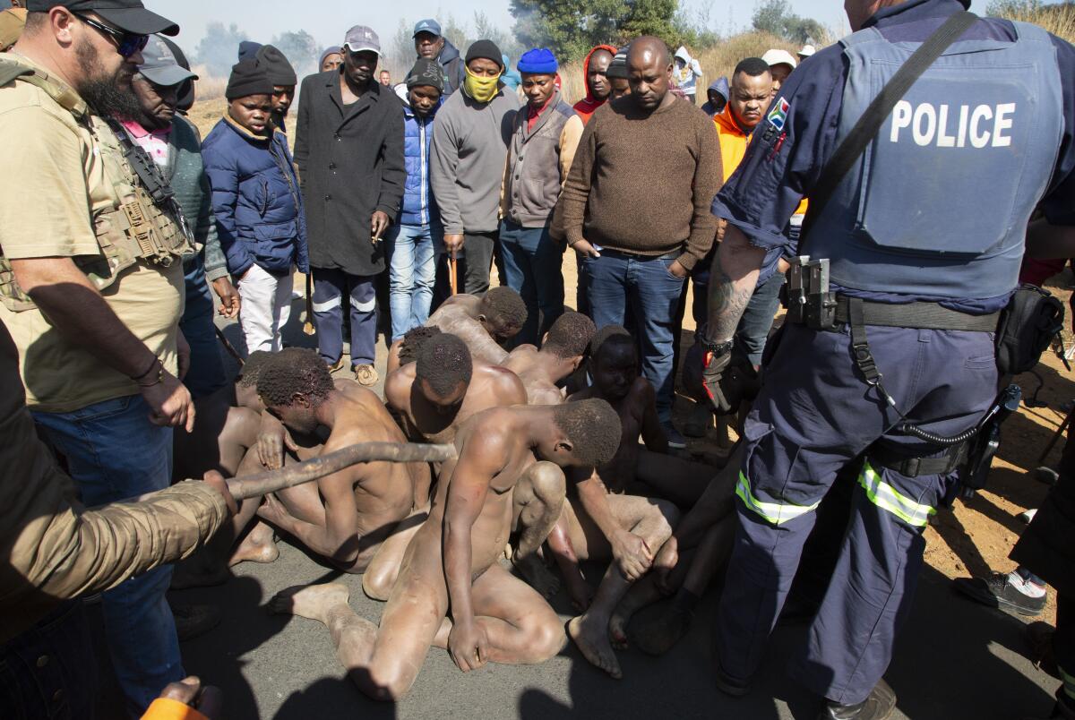 Community members look on after apprehending illegal gold miners, beating them and stripping them naked.