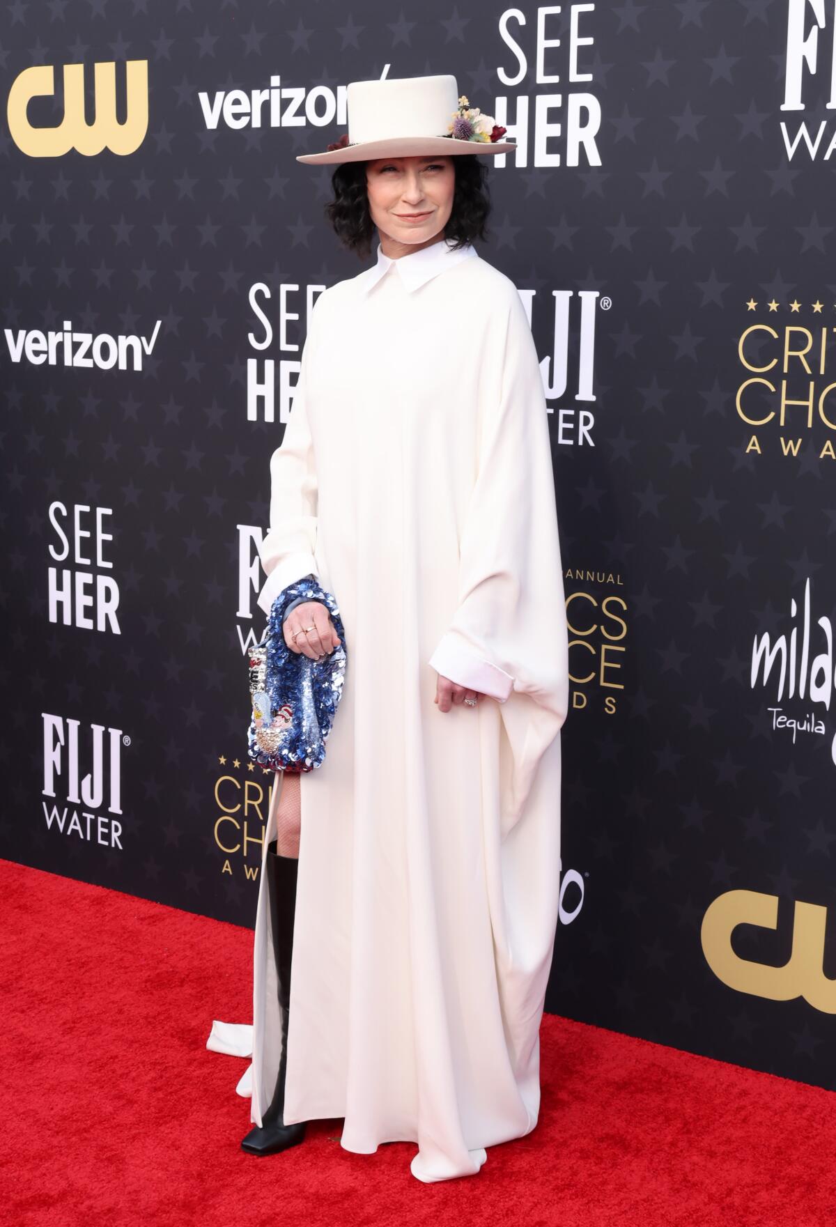 Amy Sherman-Palladino on a red carpet, in a long white dress with long sleeves and a white hat