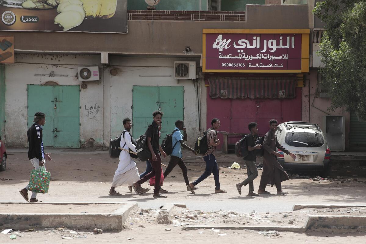 People walk past shuttered shops, including one with a sign in Arabic script
